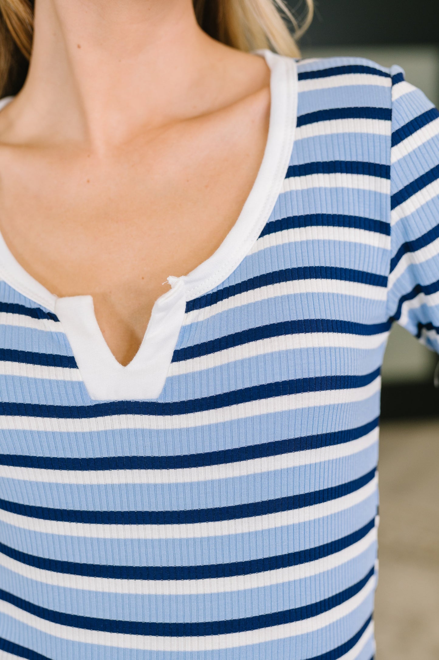 Close-up of a person wearing a ribbed short-sleeve henley top with horizontal light blue, navy, and white stripes.