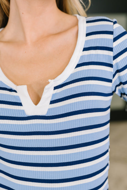 Close-up of a person wearing a ribbed short-sleeve henley top with horizontal light blue, navy, and white stripes.