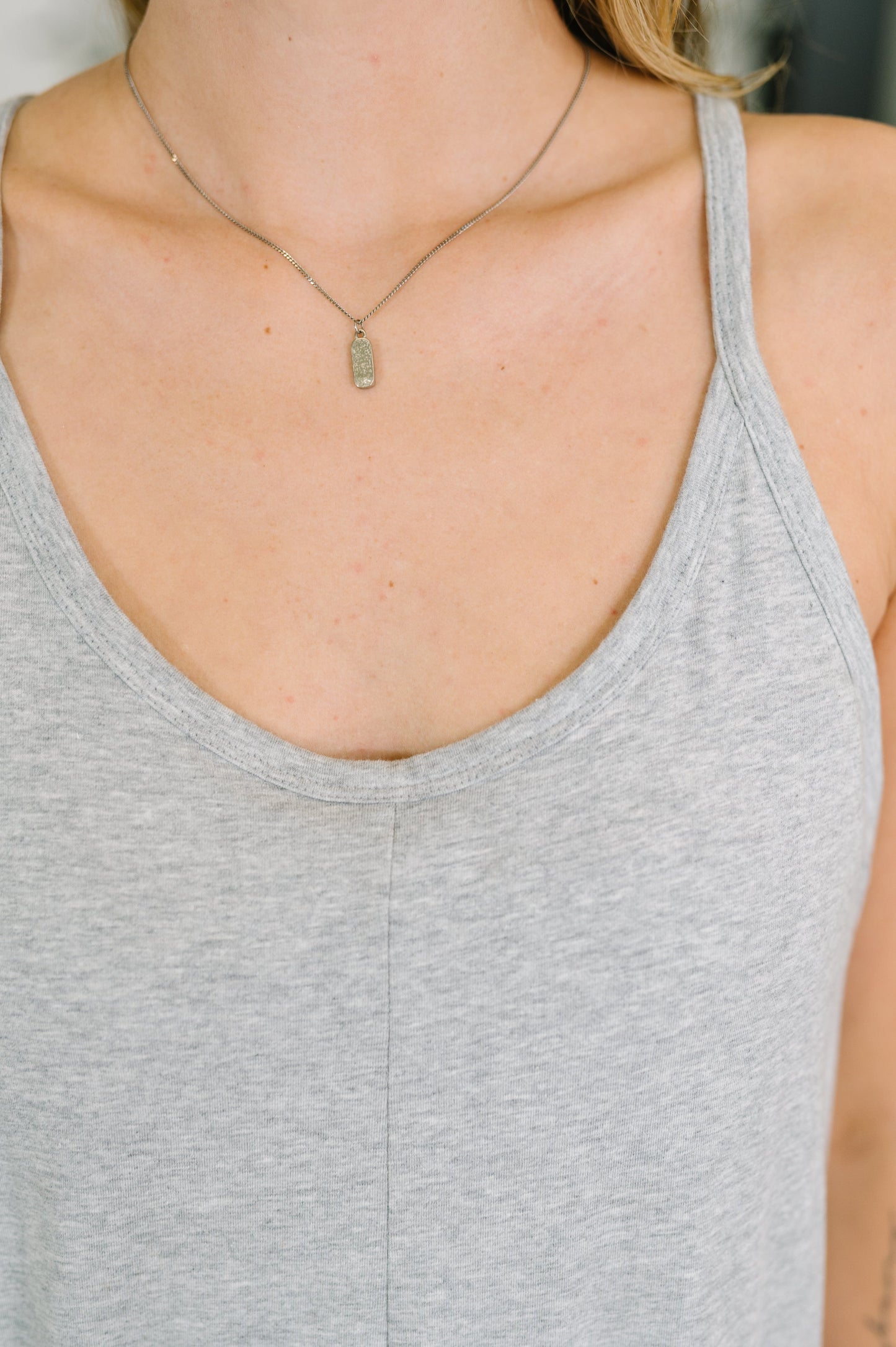 Person wearing a gray tank top and gold necklace with a pendant.