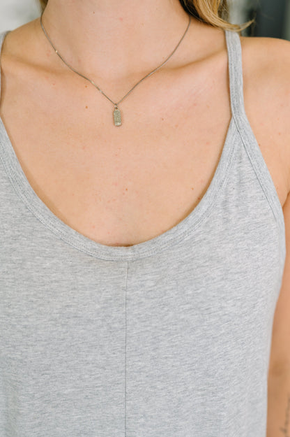 Person wearing a gray tank top and gold necklace with a pendant.