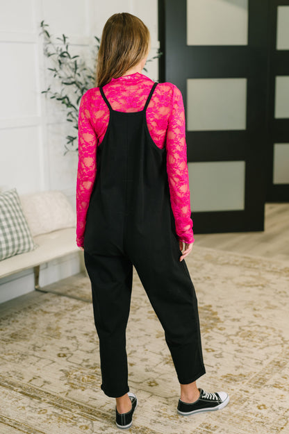 Person wearing a pink lace top and black overalls in an indoor setting.