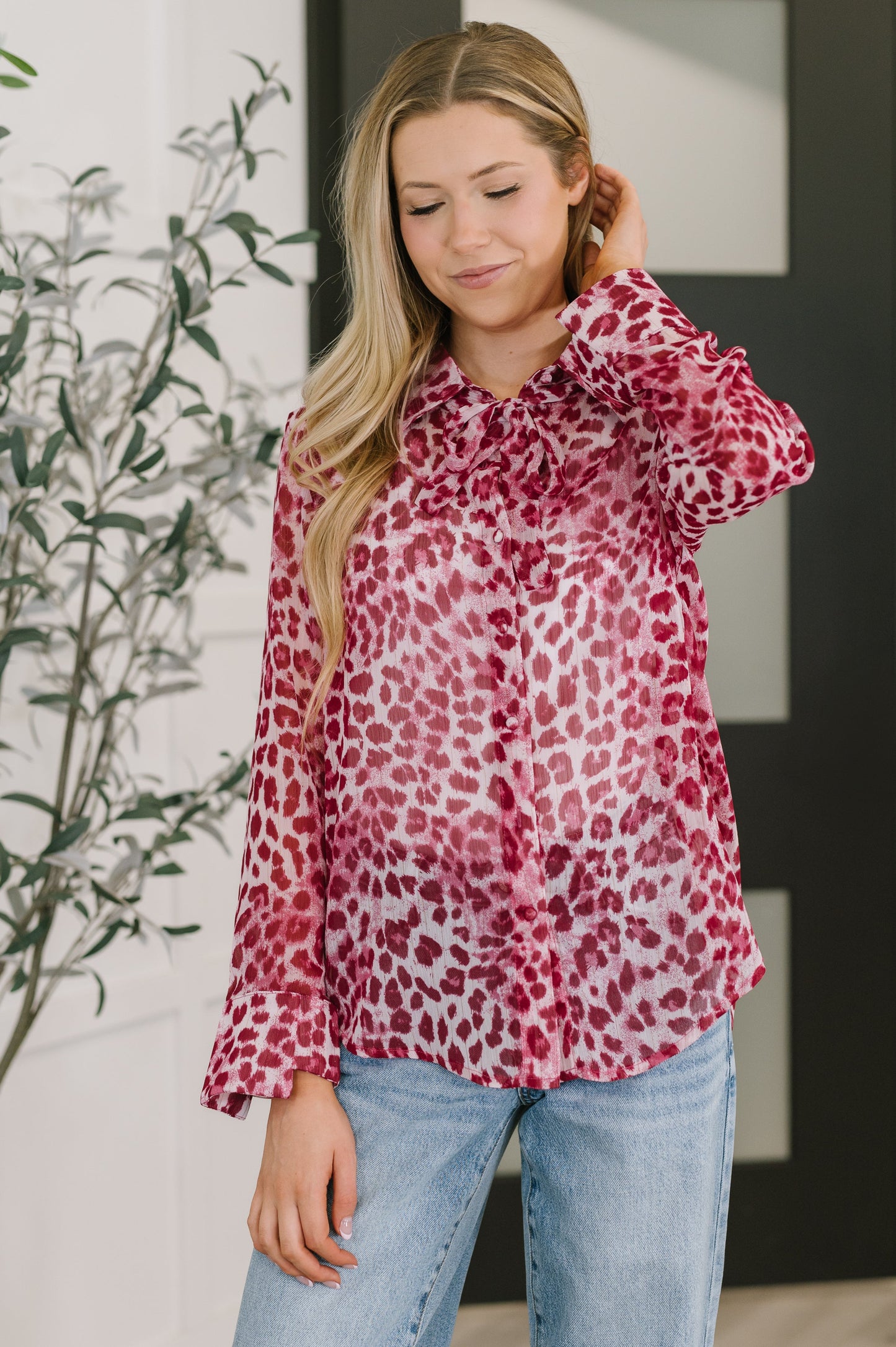 Woman wearing a red leopard print blouse with blue jeans indoors.