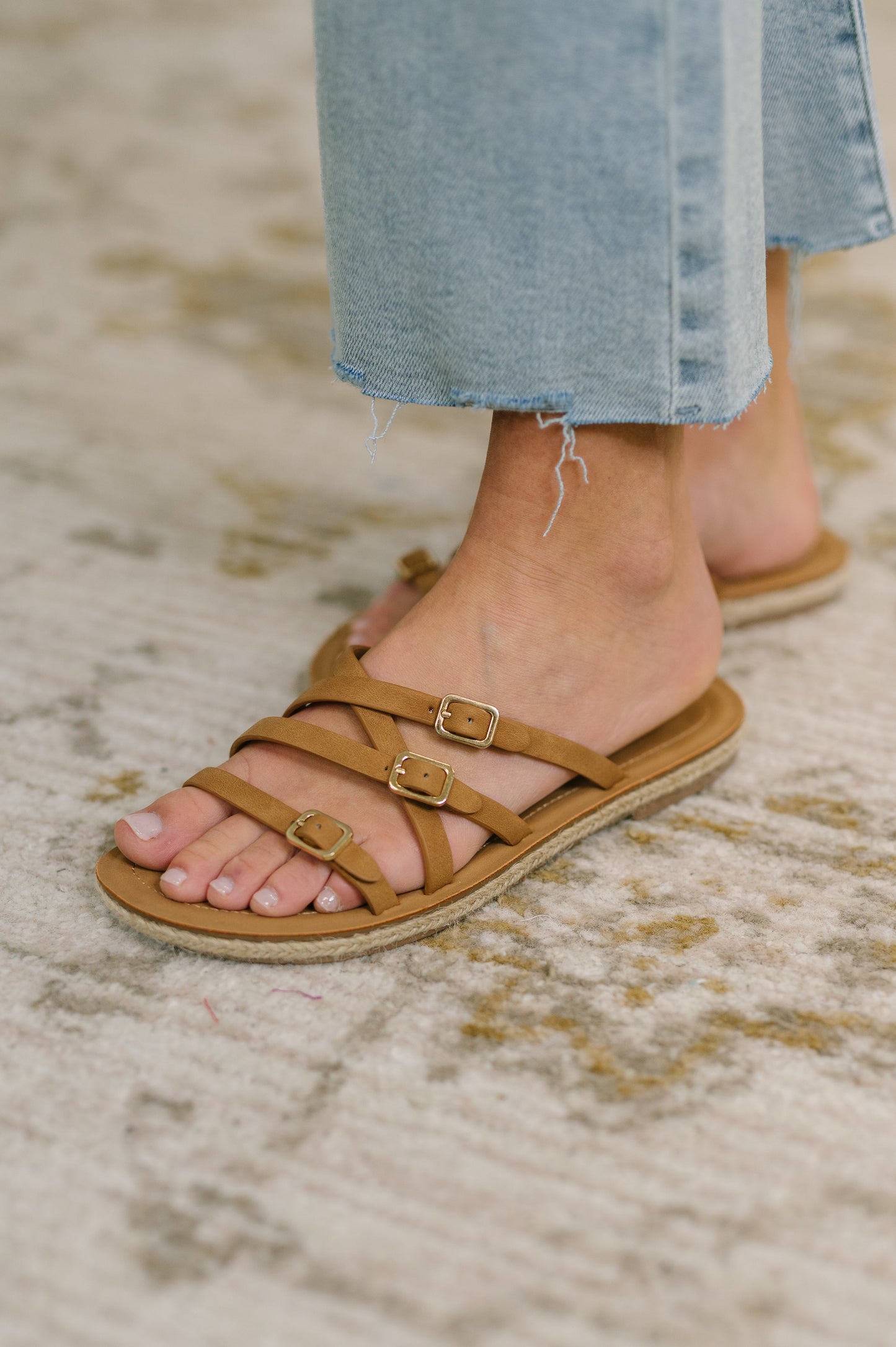 Brown sandals with buckles worn by a person on a textured surface