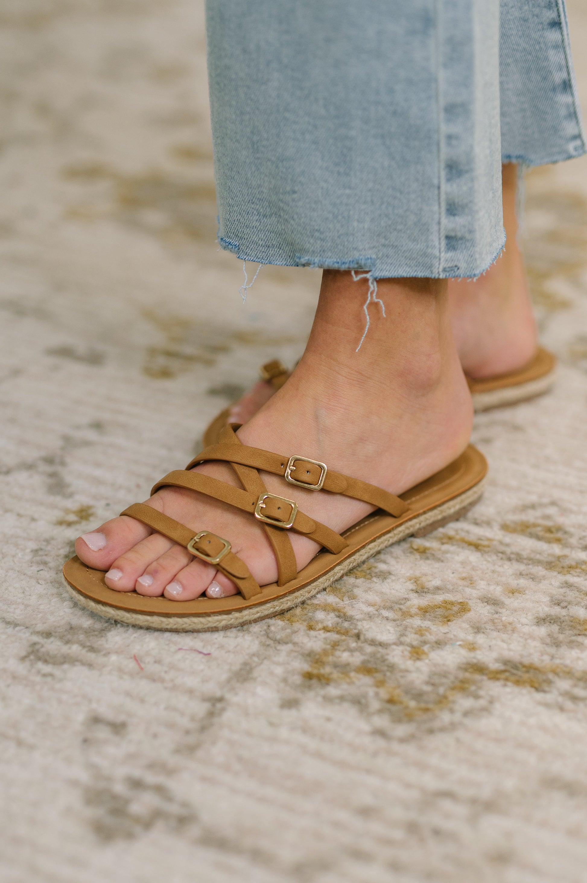 Brown sandals with buckles worn by a person on a textured surface