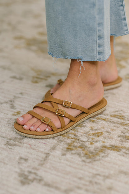 Brown sandals with buckles worn by a person on a textured surface