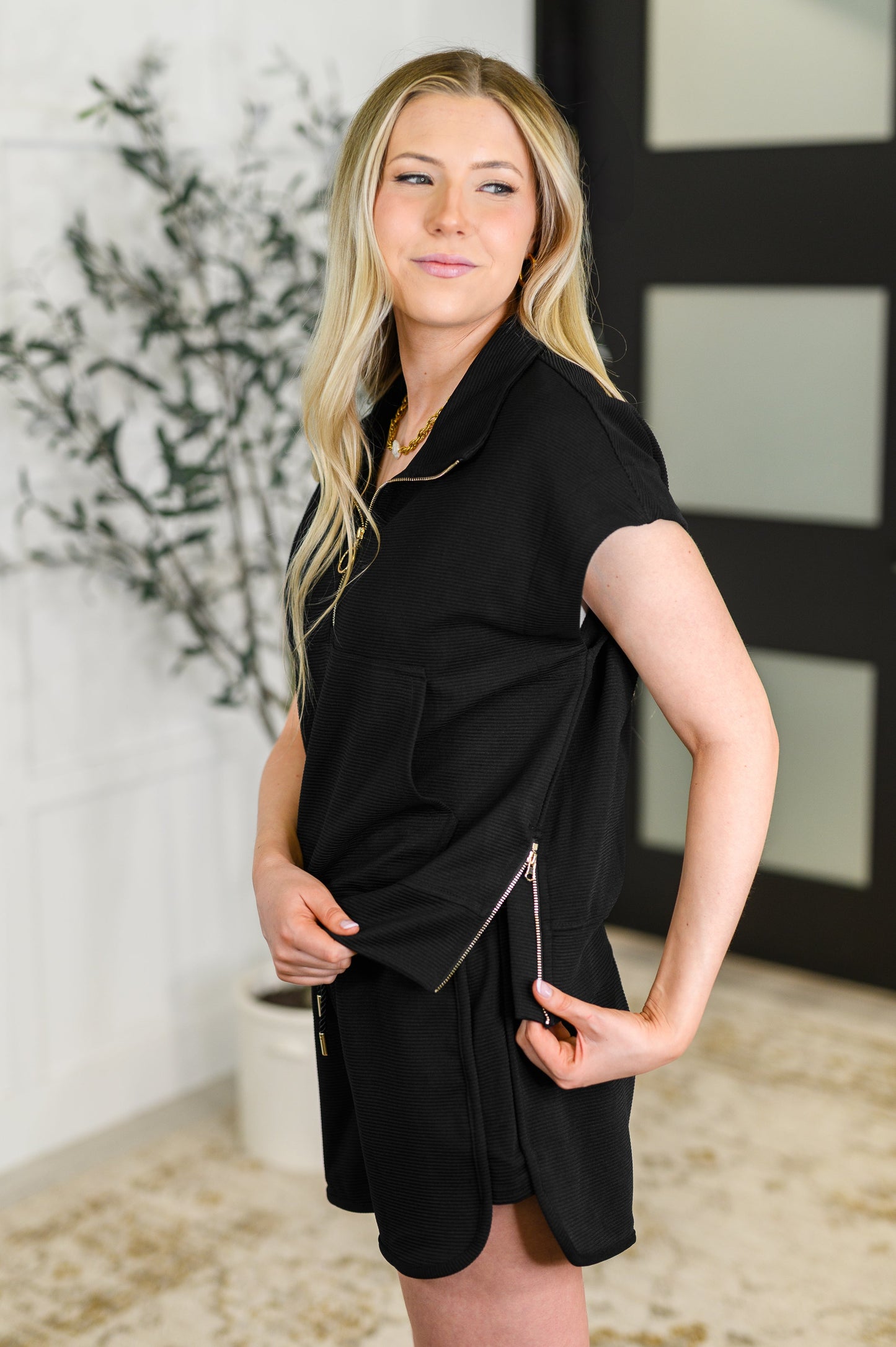 Woman wearing a black sleeveless dress with a zipper detail indoors.