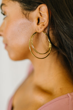 A close-up side profile of a woman wearing a pair of thick, double-layered gold hoop earrings.