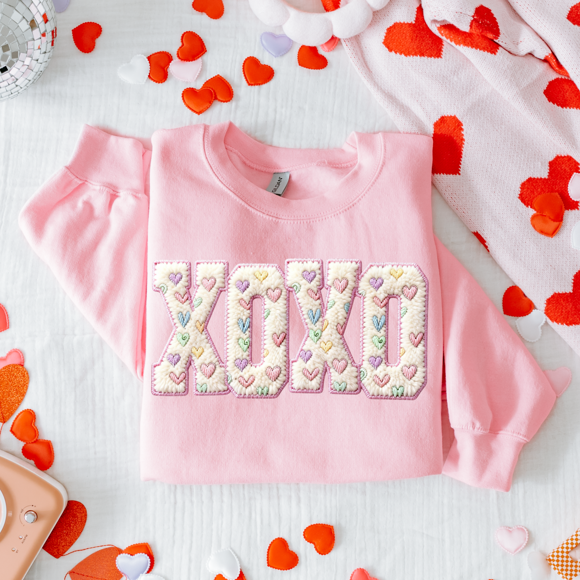 Pink sweatshirt with 'XOXO' design surrounded by heart-shaped decorations on a white background