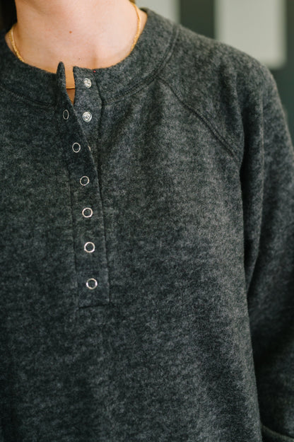Close-up of a person wearing a black henley button-up shirt.
