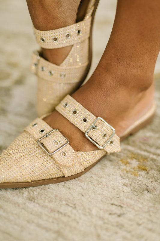 Beige flat shoes with buckle details worn by a person on a textured surface