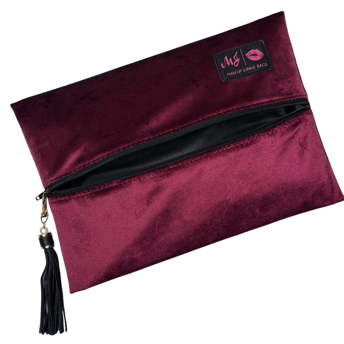 A burgundy velvet makeup bag with a black zipper, a black tassel charm, and a black brand patch on the top right.