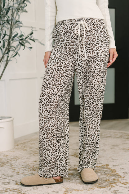 Person wearing leopard print pants in a room with a plant and rug.