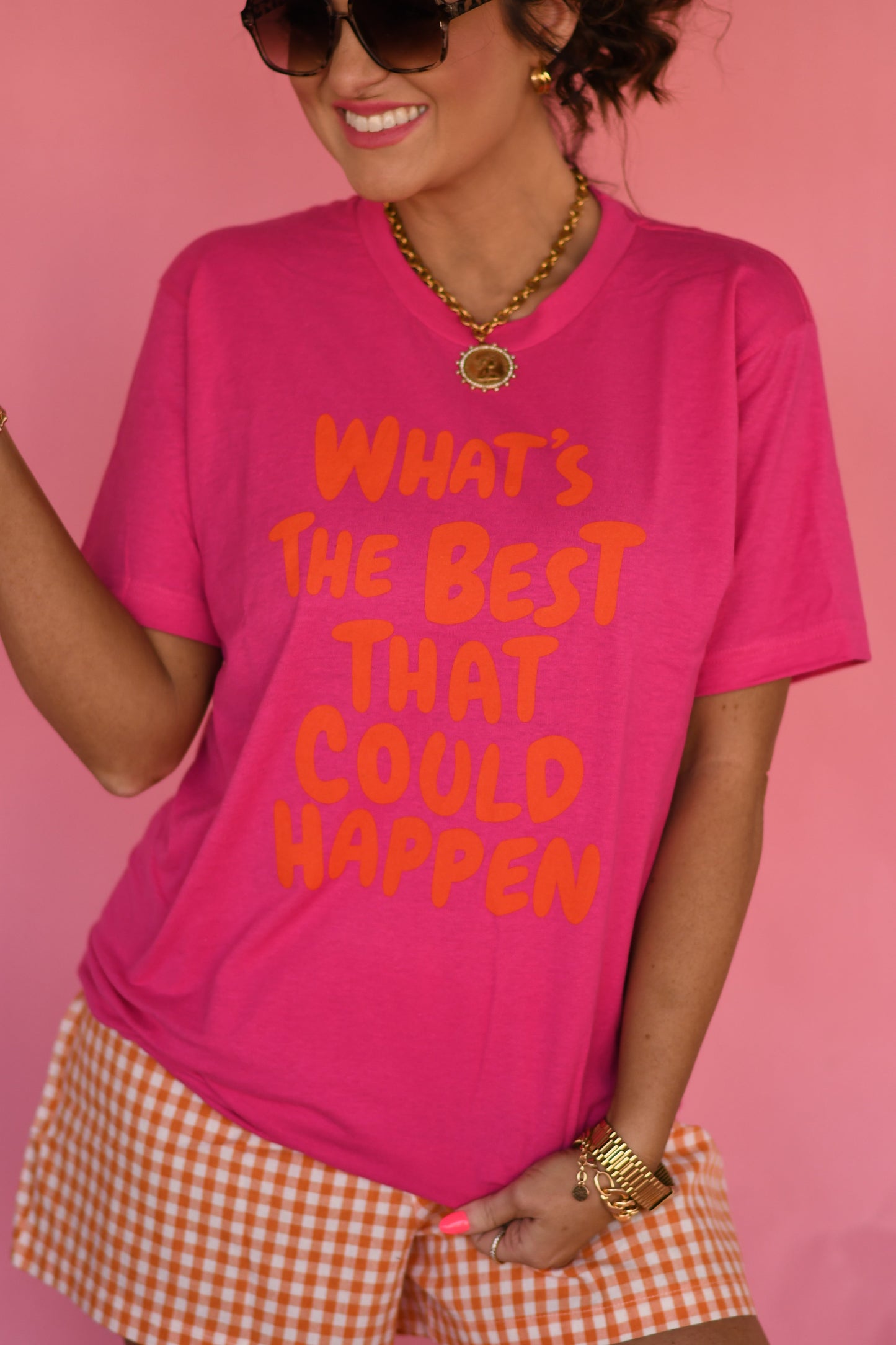 Person wearing a pink t-shirt with text and checkered shorts against a pink background