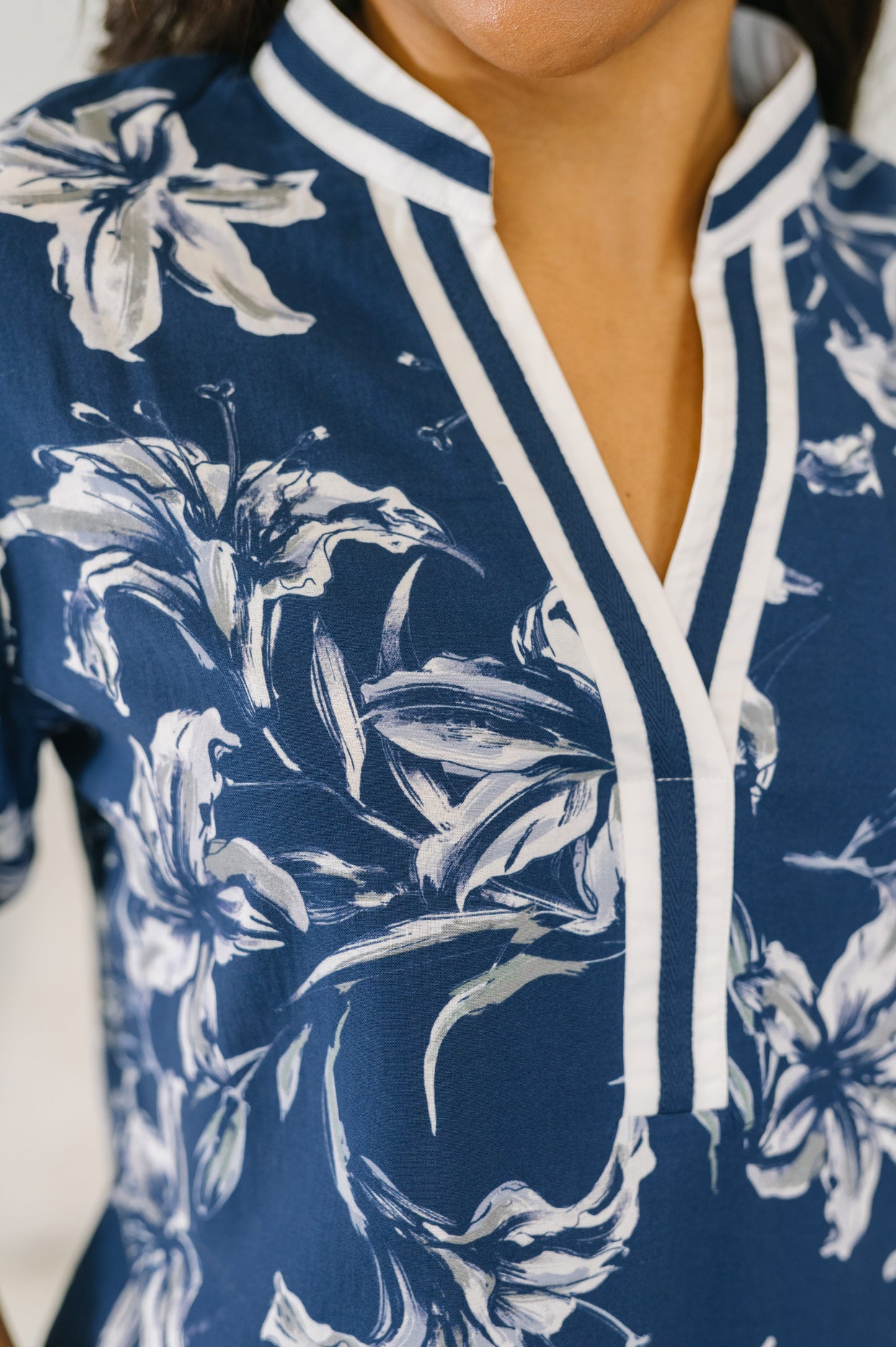 Close-up of a navy blue floral top with a white lily print and white striped trim on a V-neckline.