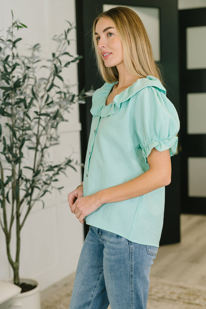 Woman wearing a light blue blouse with ruffled details and blue jeans indoors.