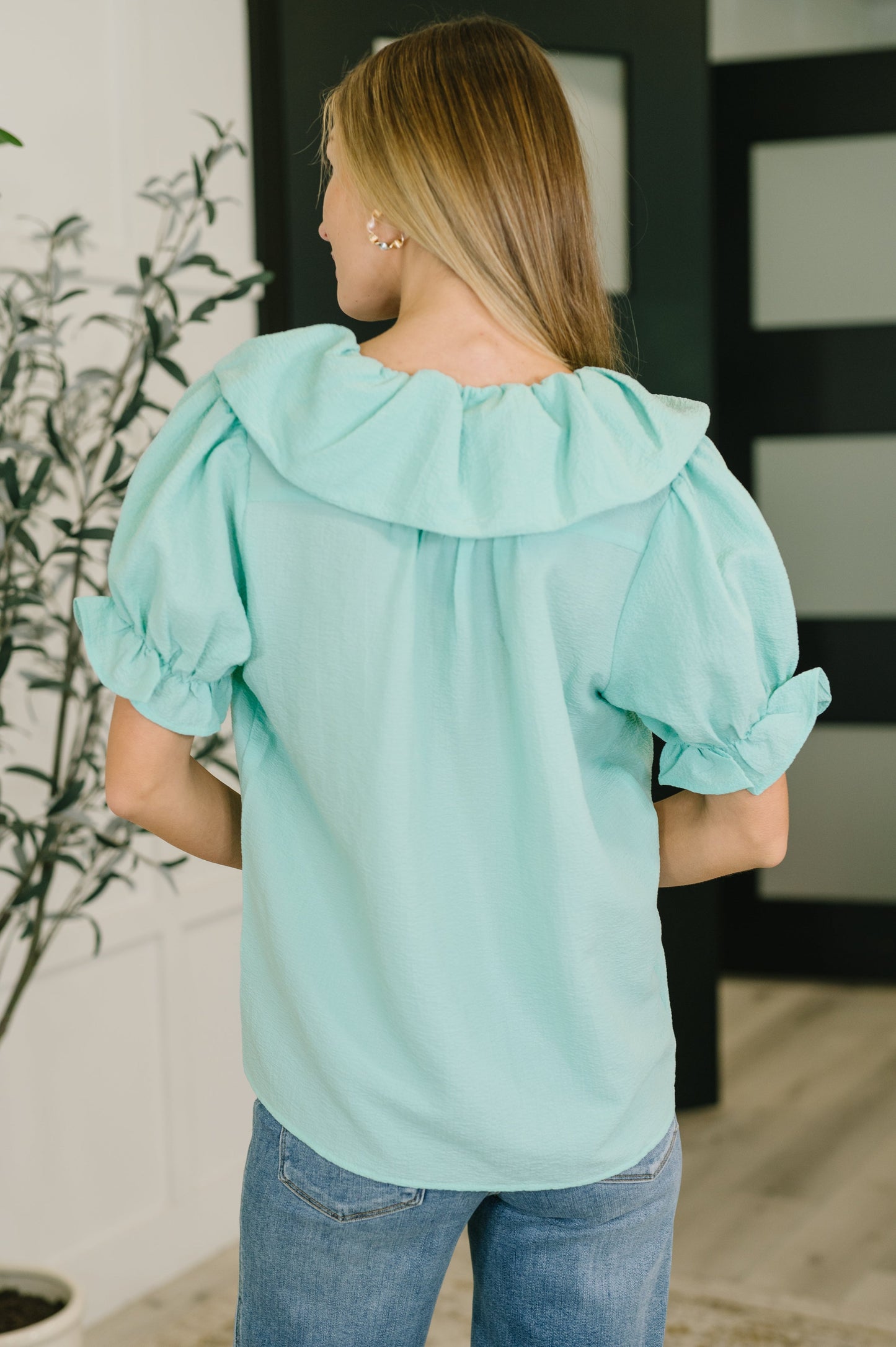 Woman wearing a light blue blouse with ruffled sleeves in an indoor setting.