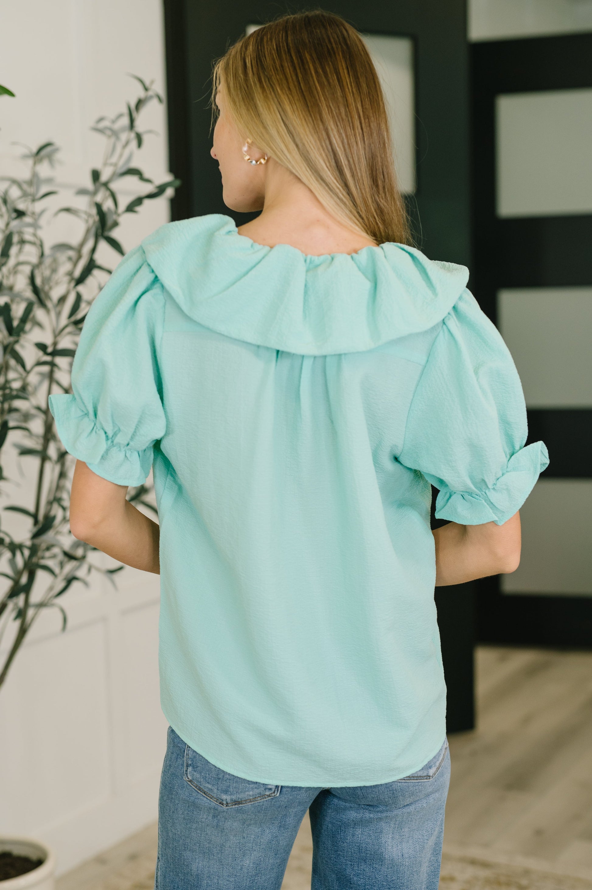 Woman wearing a light blue blouse with ruffled sleeves in an indoor setting.