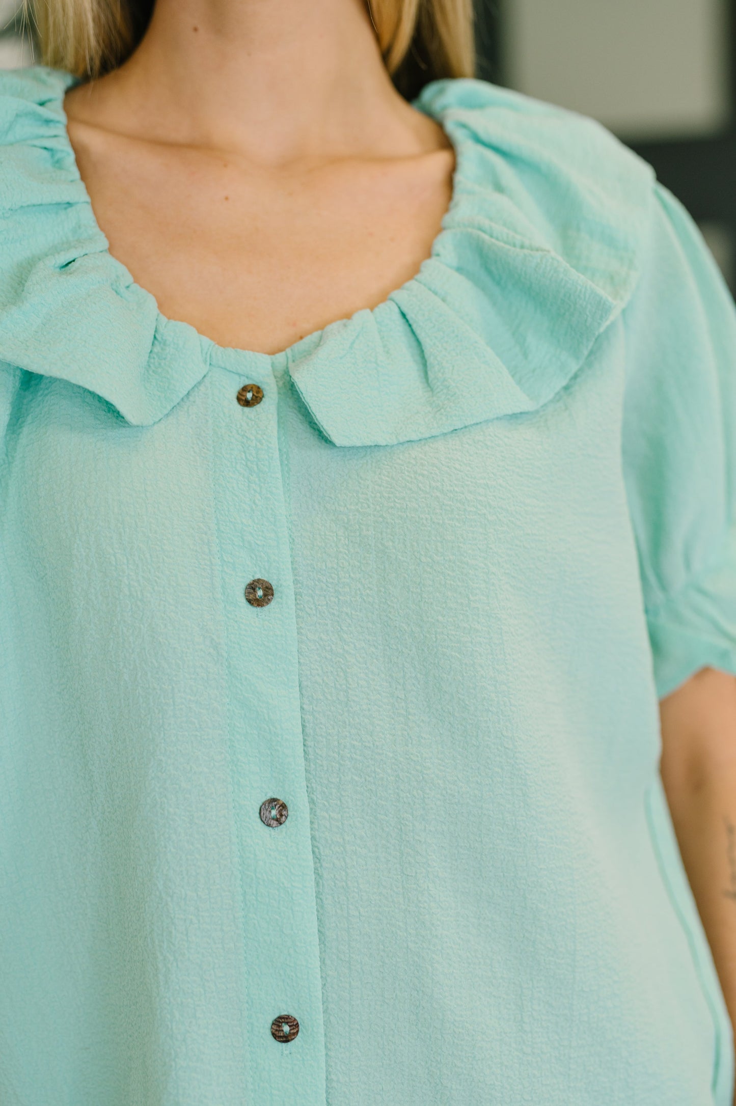 Close-up of a light blue blouse with ruffled collar and buttons.