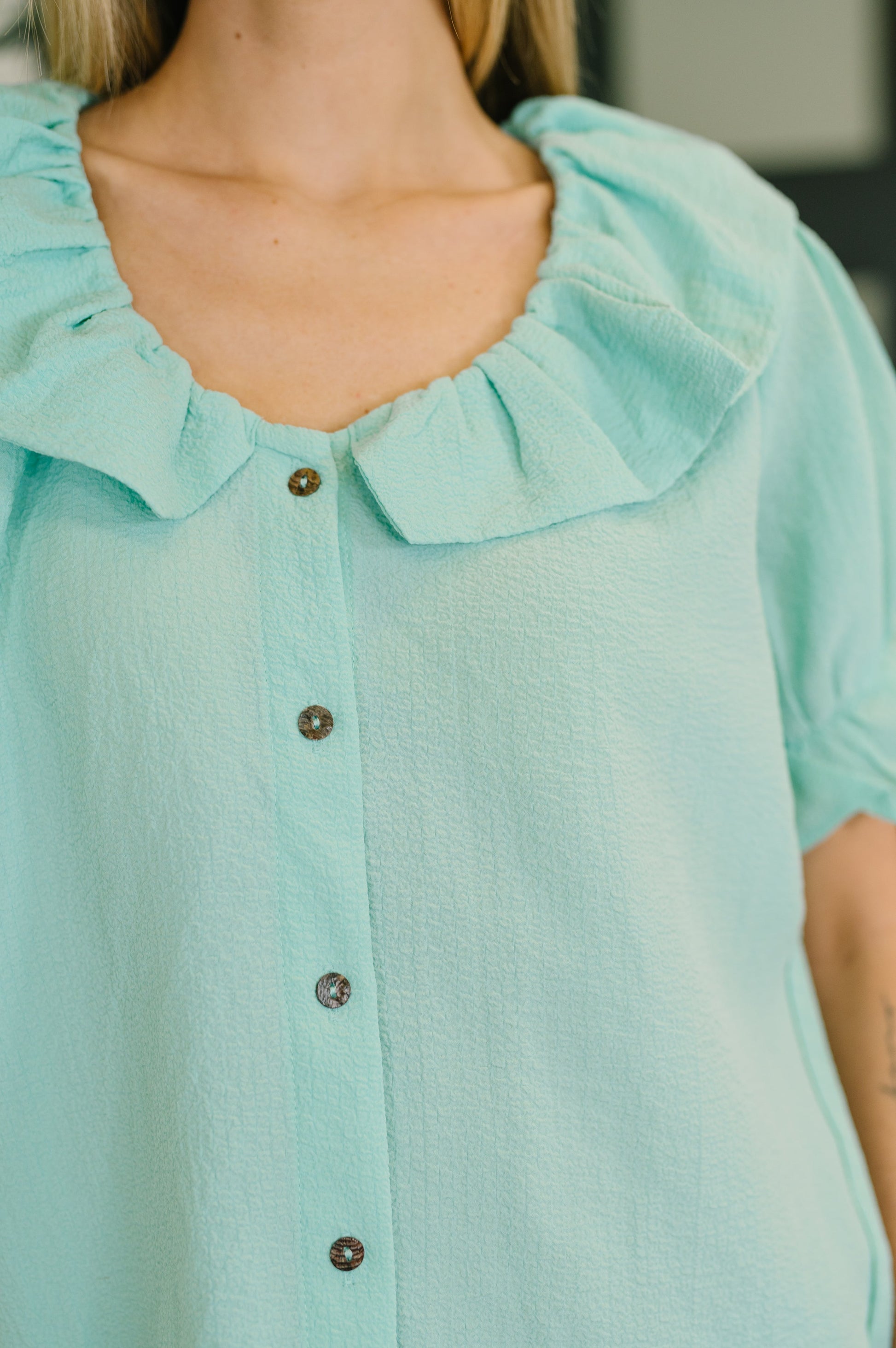 Close-up of a light blue blouse with ruffled collar and buttons.