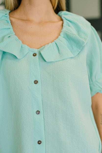 Close-up of a light blue blouse with ruffled collar and buttons.