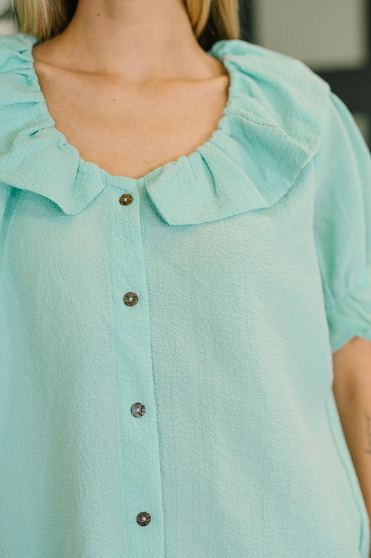 Close-up of a light blue blouse with ruffled collar and buttons.