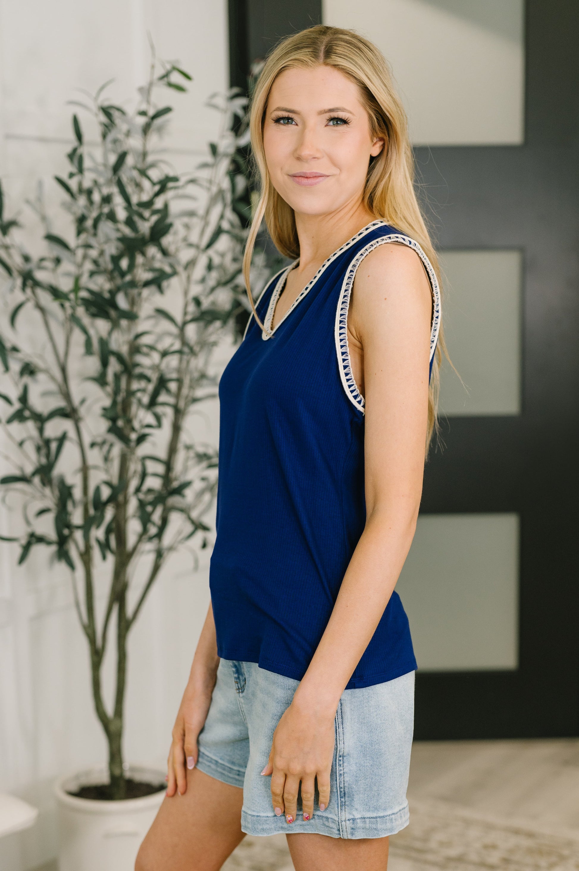 Woman wearing a blue sleeveless top with white trim in an indoor setting.