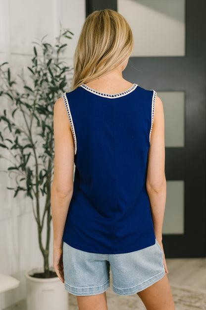 Woman wearing a blue sleeveless top with white trim and denim shorts indoors.