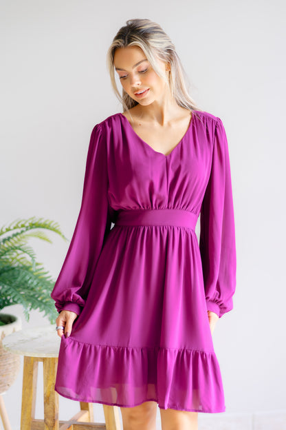 Woman wearing a purple dress with long sleeves in an indoor setting.