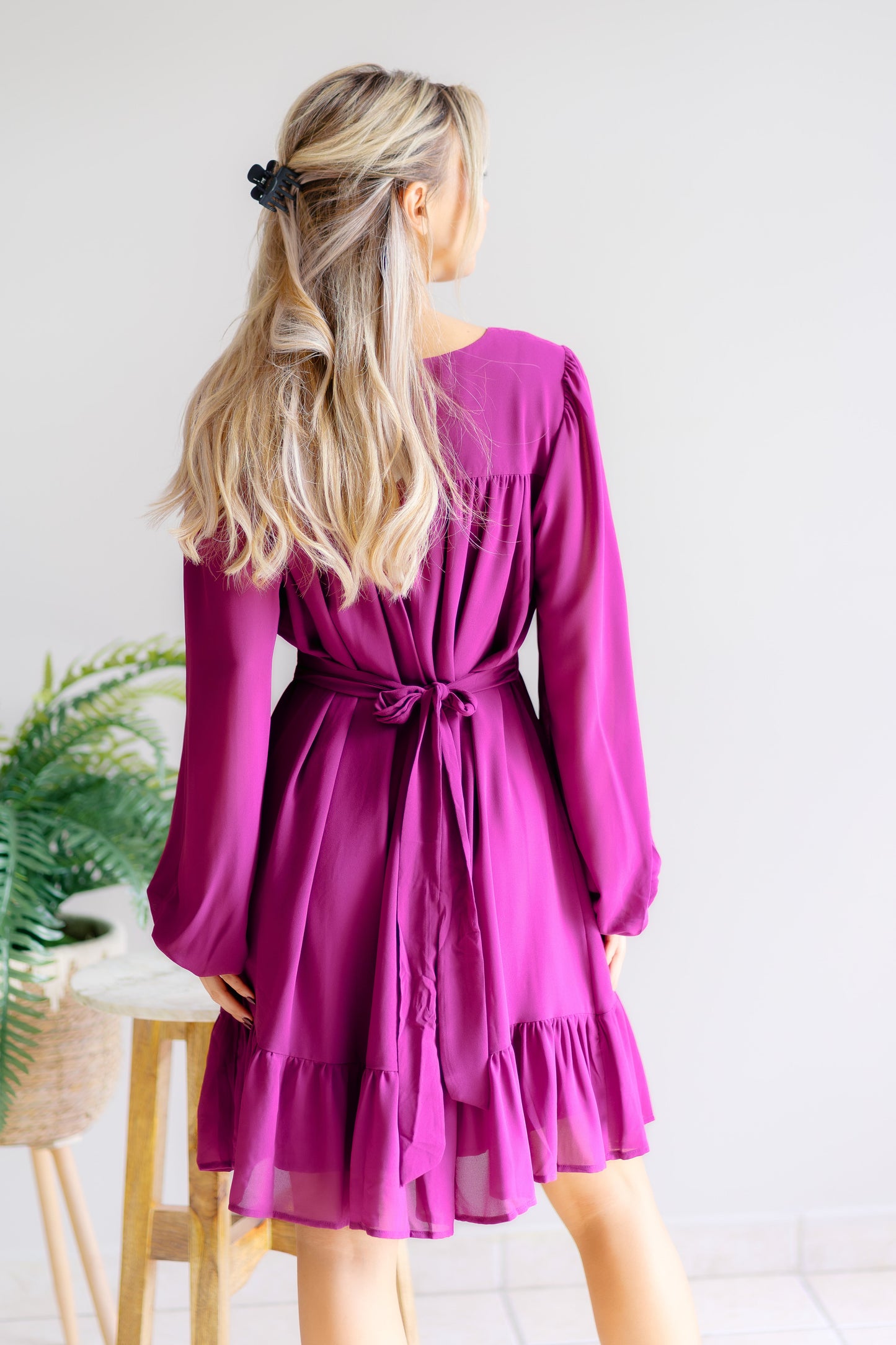 Woman wearing a purple dress with long sleeves in a minimal indoor setting.