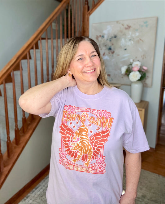 Woman wearing a purple t-shirt with a colorful graphic design indoors.