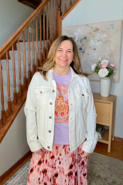 Woman standing in a home setting with a staircase and floral decorations.