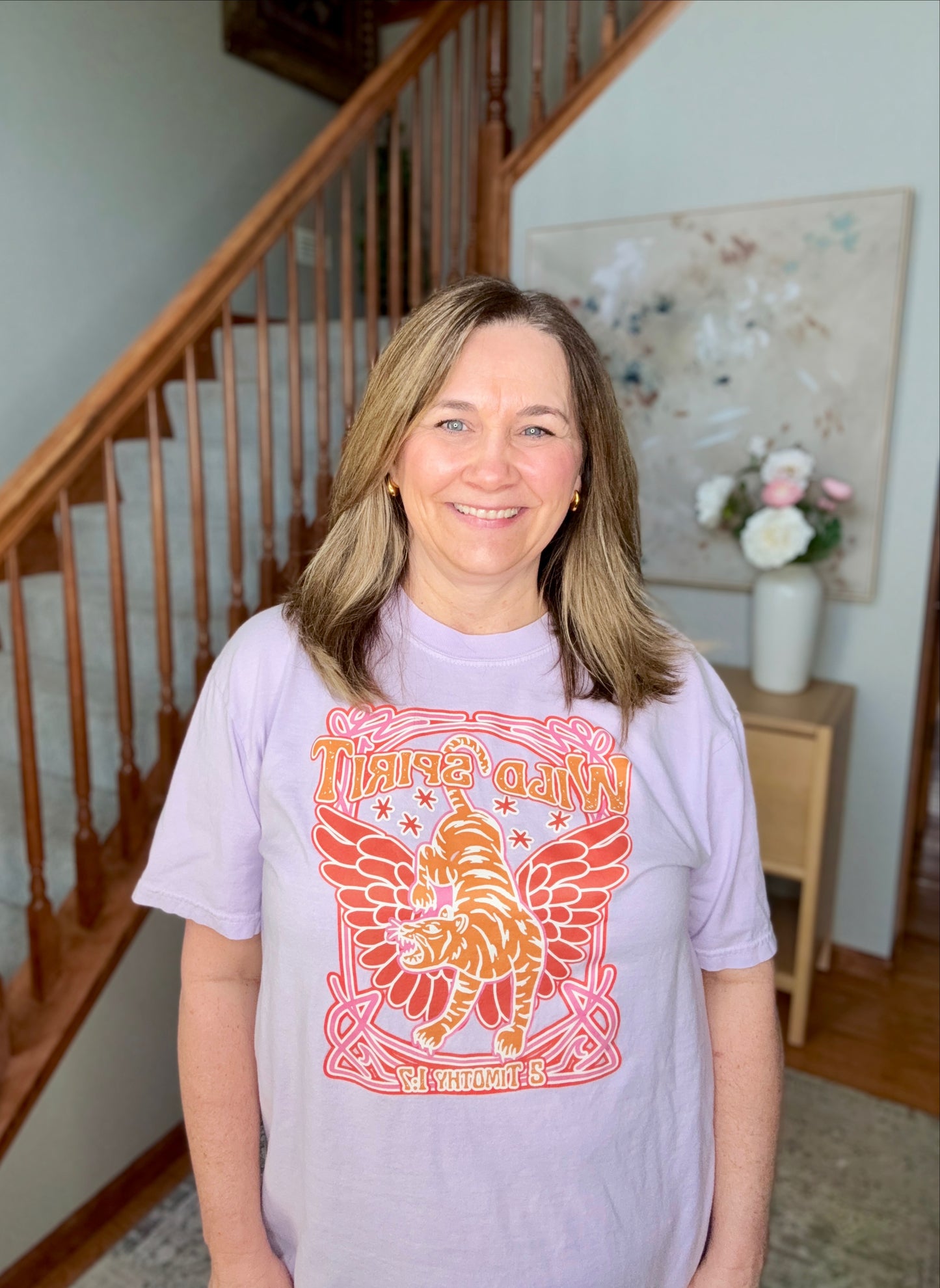 Woman wearing a purple t-shirt with a colorful graphic design in a home setting.