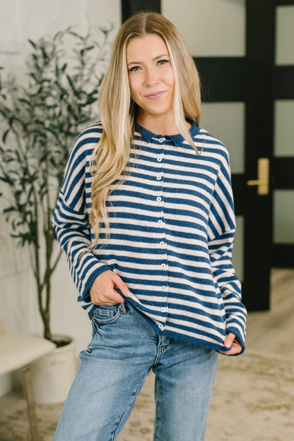 A woman wearing a navy blue and white striped long-sleeve button-up shirt with a polo collar, paired with light-wash blue jeans, standing in an indoor setting.