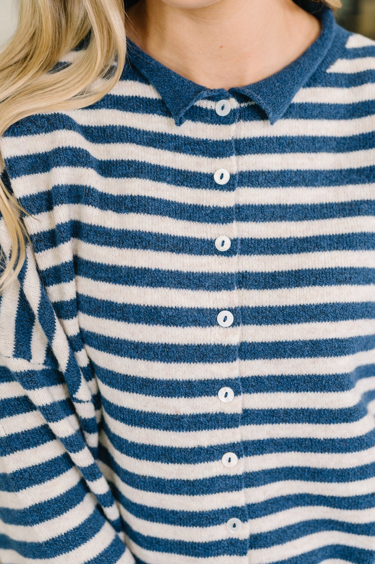 Close-up of a person wearing a blue and white striped knit polo shirt with white buttons.