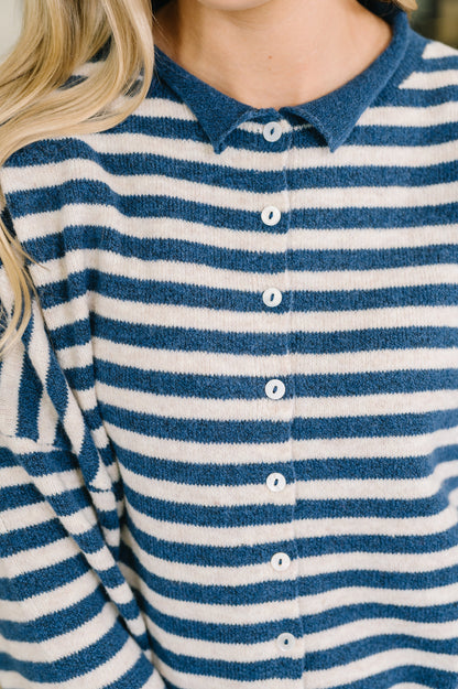 Close-up of a person wearing a blue and white striped knit polo shirt with white buttons.