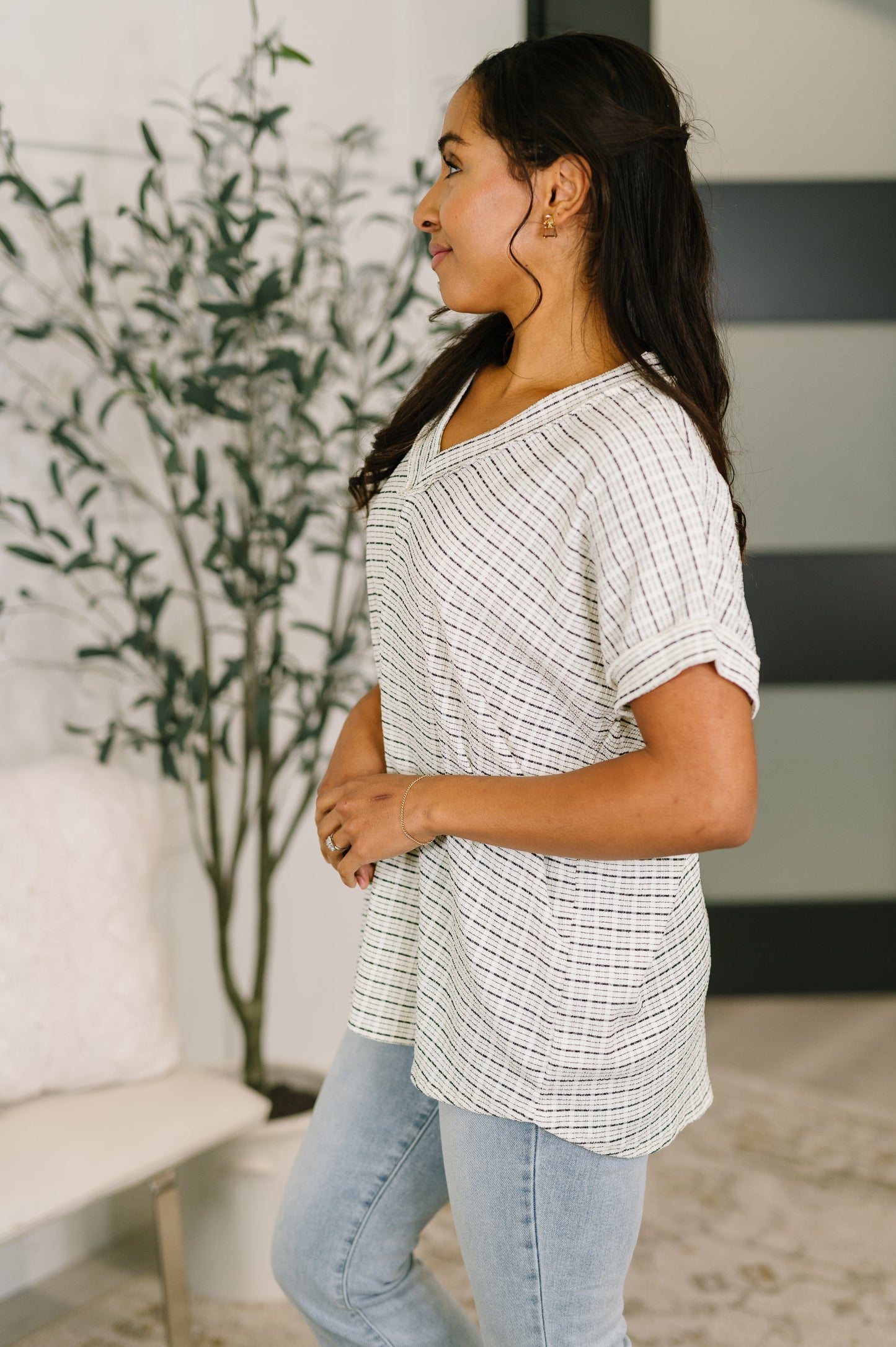 Woman wearing a checkered shirt and jeans standing in a room with a plant and furniture.