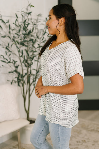 Woman wearing a checkered shirt and jeans standing in a room with a plant and furniture.