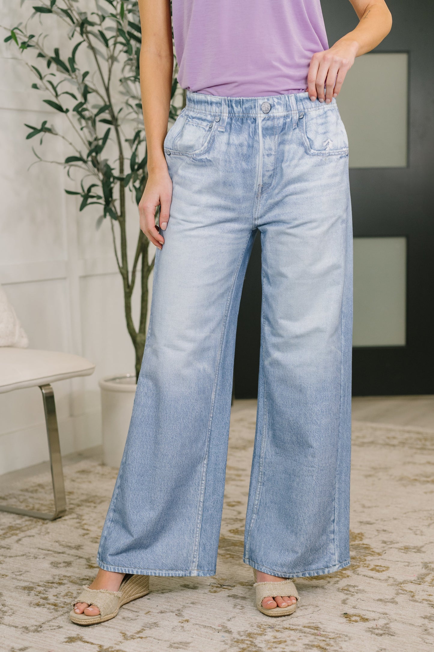 Person wearing light blue wide-leg jeans and a purple top indoors.