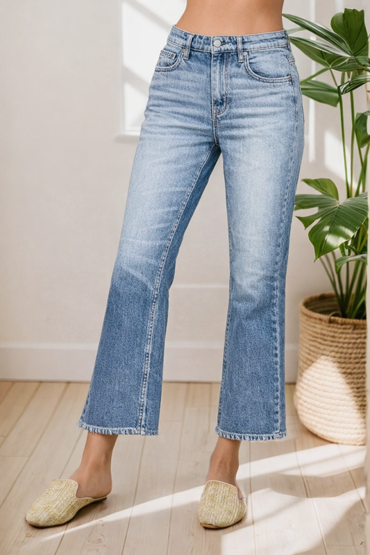 Person wearing light blue jeans standing indoors with a plant in the background