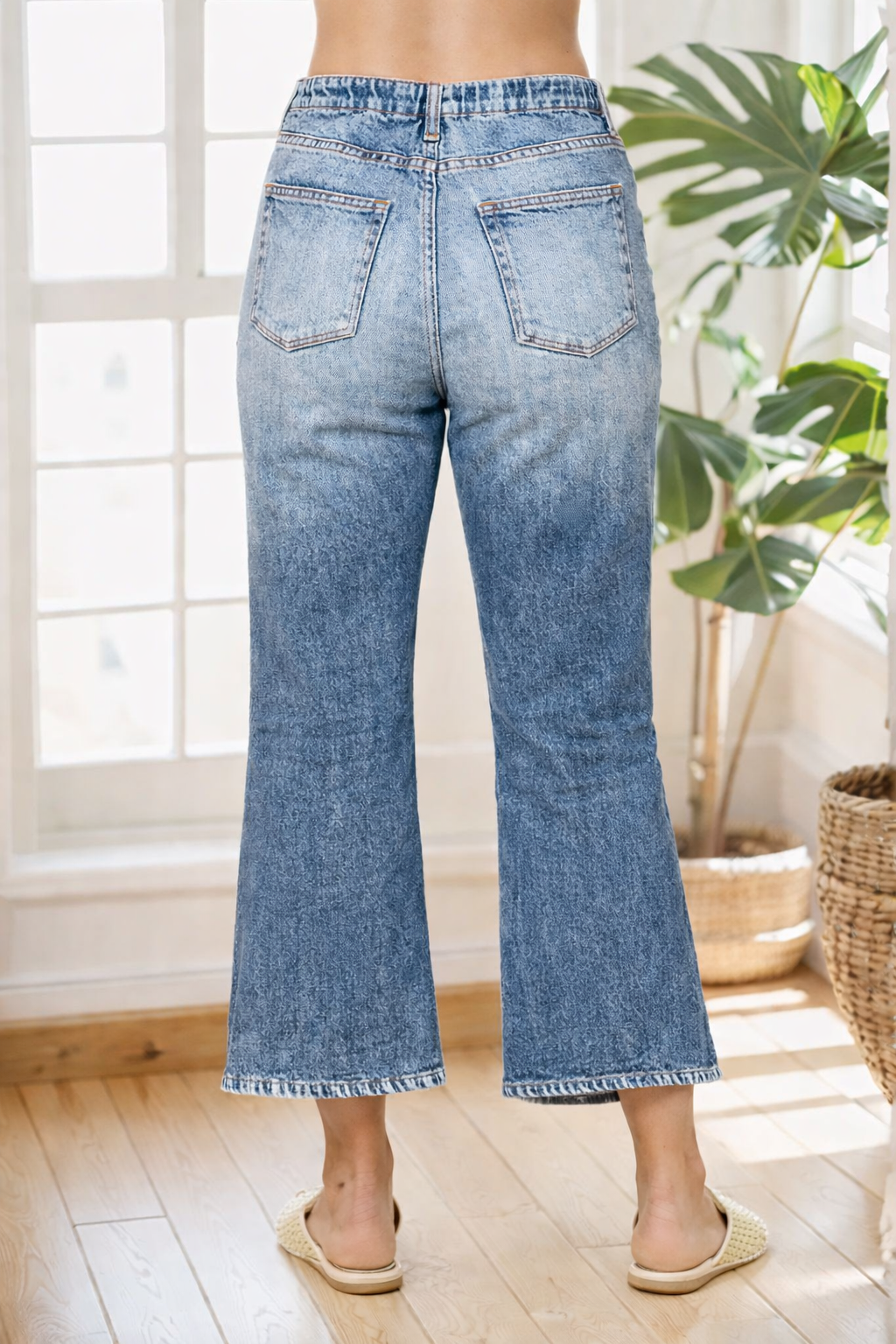 Person wearing light blue jeans standing in a room with a plant and window in the background
