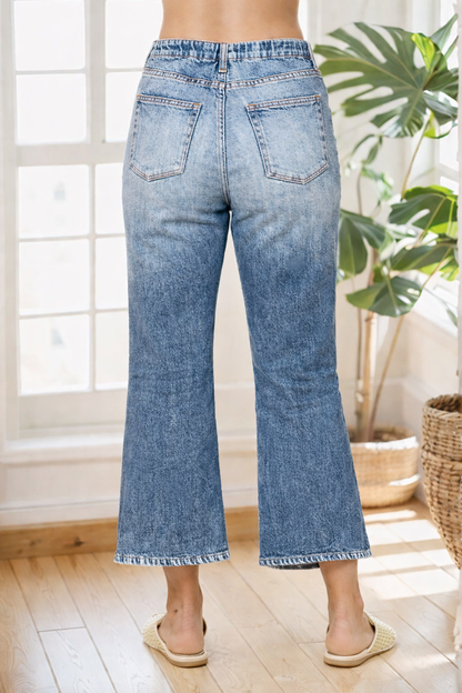 Person wearing light blue jeans standing in a room with a plant and window in the background