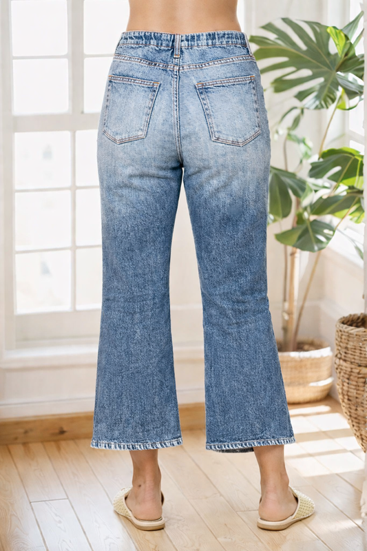 Person wearing light blue jeans standing in a room with a plant and window in the background