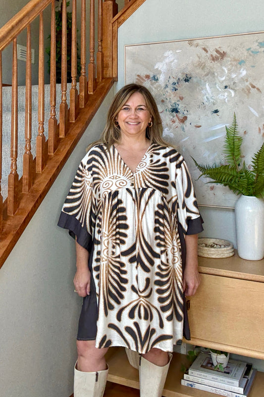 Woman in a patterned dress standing in a home interior with a staircase and decor.