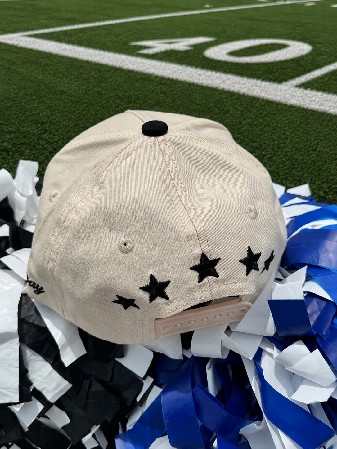 Beige cap with star patterns on a football field with pom-poms