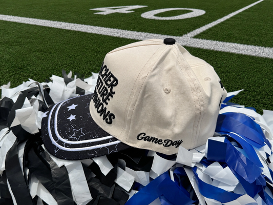 Beige cap with 'Game Day' text on a football field with pom-poms.