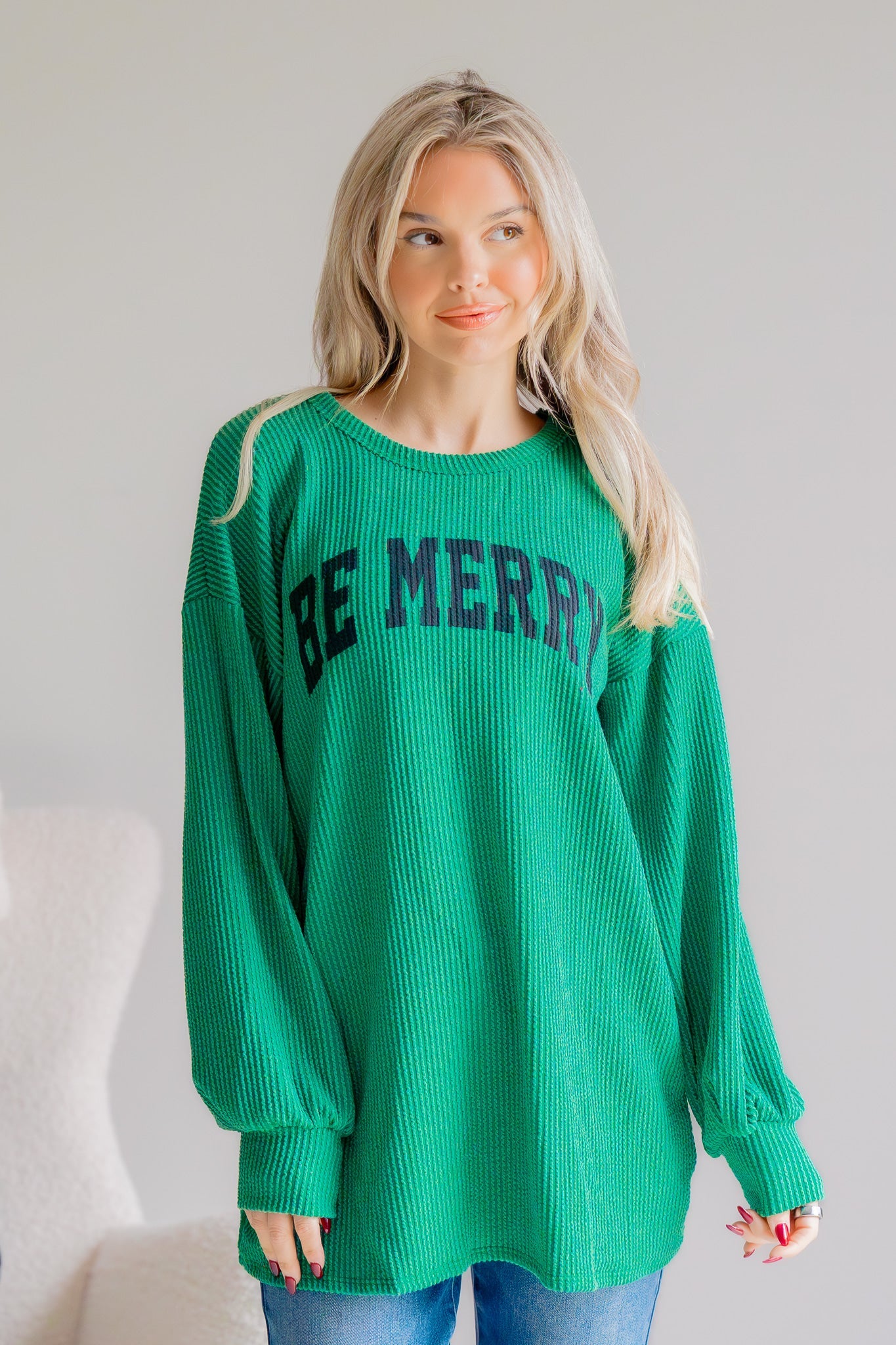 Woman wearing a green sweater with 'BE MERRY' text against a plain background