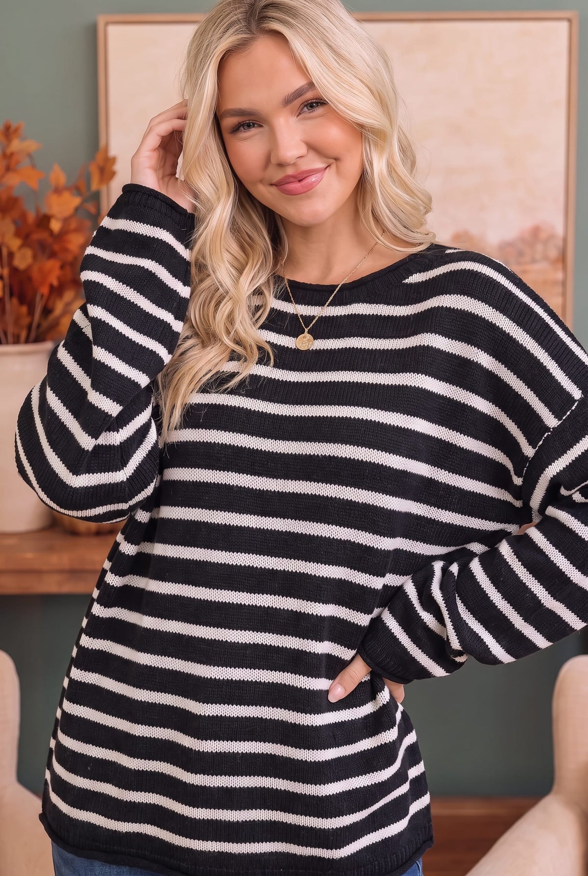 A woman wearing a black and white horizontally striped knit sweater, posing in an indoor setting with a framed picture and autumn decor in the background.