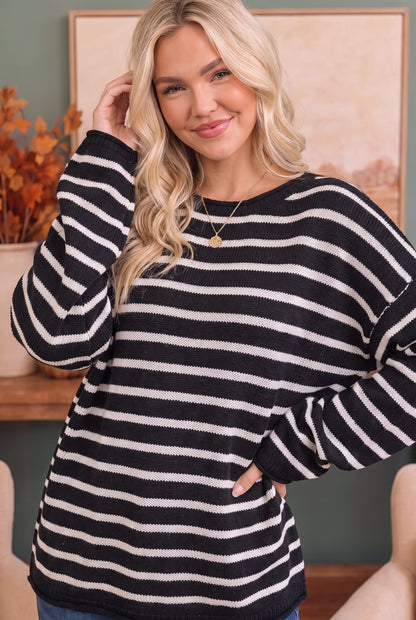 A woman wearing a black and white horizontally striped knit sweater, posing in an indoor setting with a framed picture and autumn decor in the background.