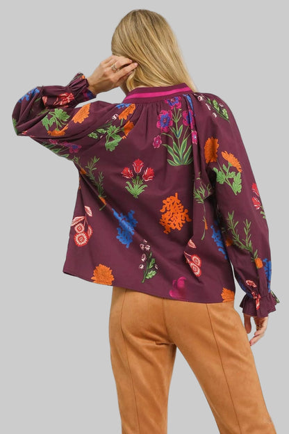 Person wearing a burgundy floral blouse with colorful patterns on a white background