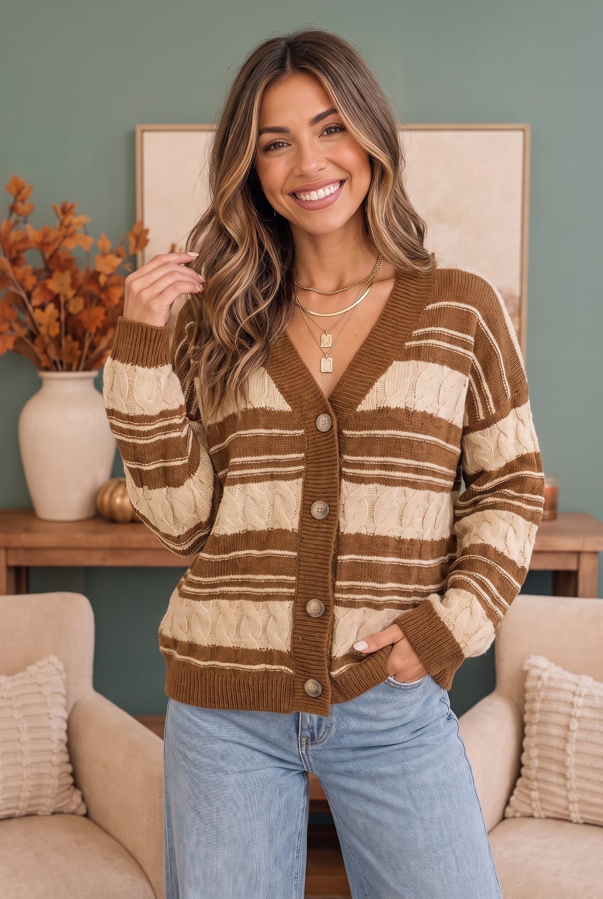 A woman wearing a brown and cream striped cardigan sweater with light blue jeans, standing in a cozy living room setting.
